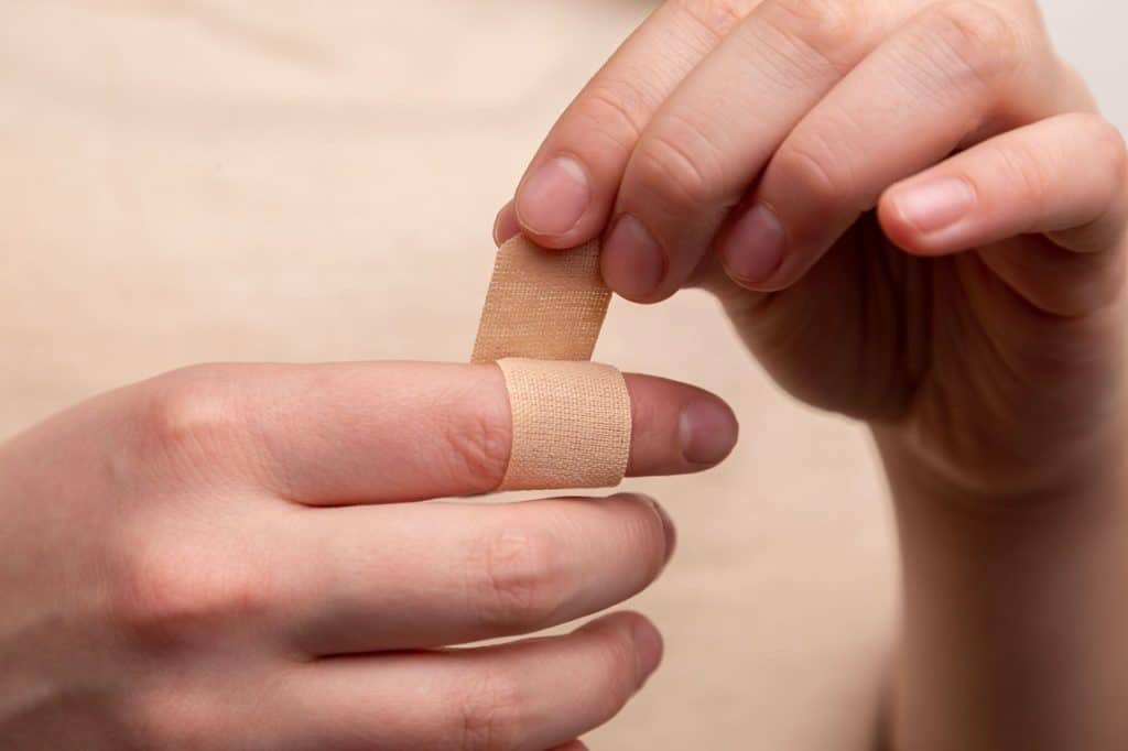 A person applies a bandage to their finger, using both hands.