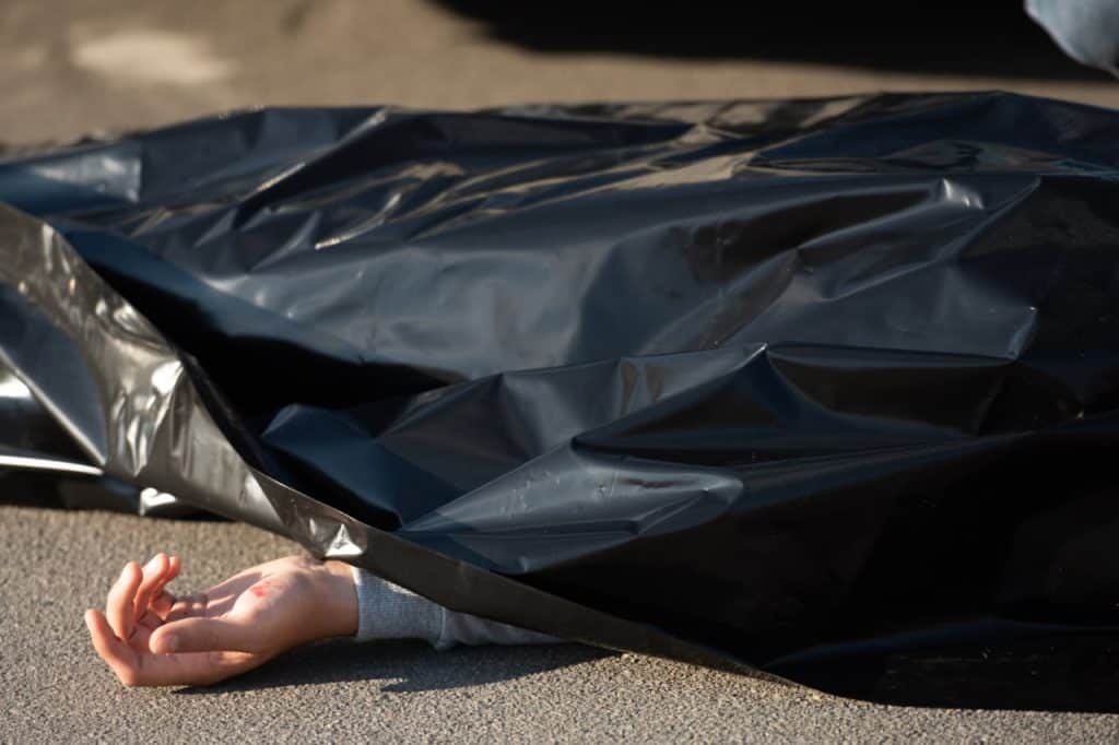 A hand protrudes from underneath a black plastic sheet, resting on a concrete surface.