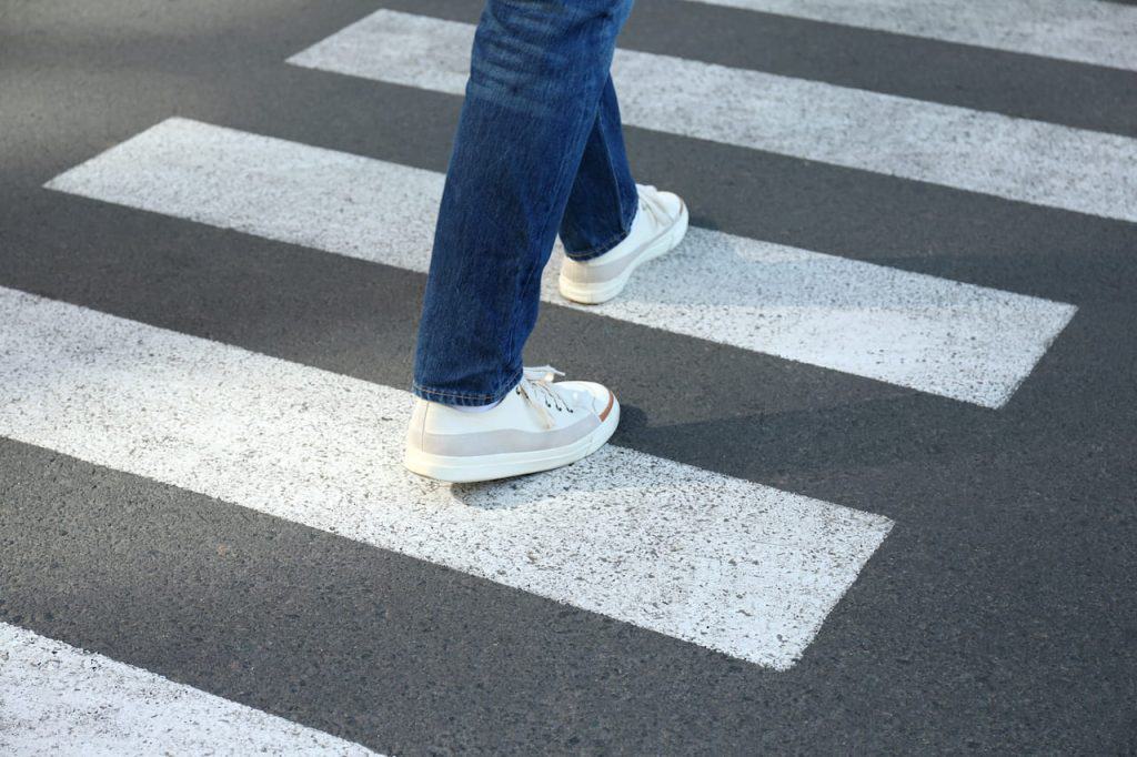 Person walking in white sneakers and blue jeans on a zebra crossing.