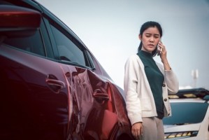 Young woman standing beside damaged car after collision on roadside