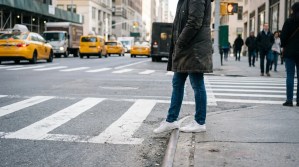 pedestrian standing at crosswalk curb on busy urban street with taxis