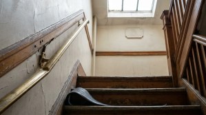 worn wooden staircase with loose peeling floor material and damaged handrail bracket