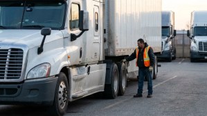 truck driver in safety vest inspecting semi-truck tires in commercial lot